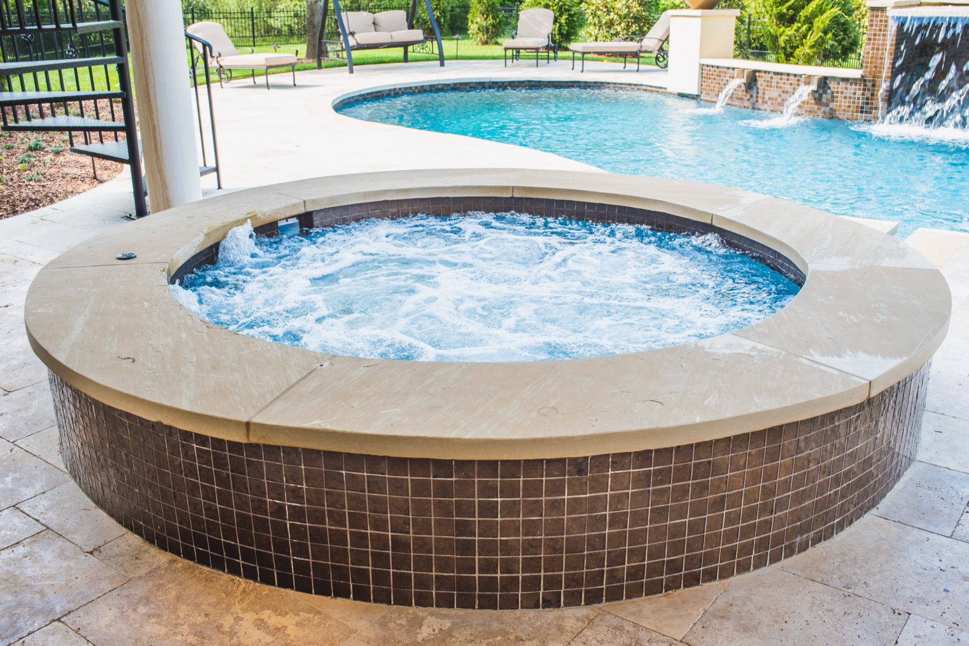 Round bubbling spa with mosaic tile and pool waterfall in Nashville backyard